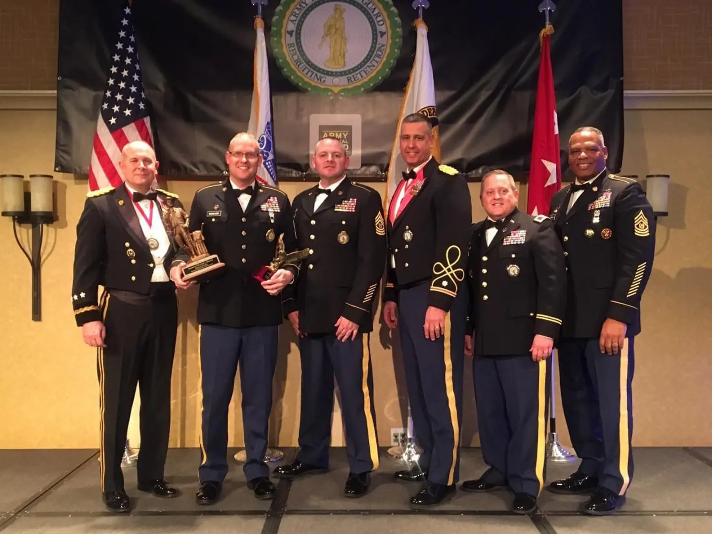 Military personnel posing with awards on stage.